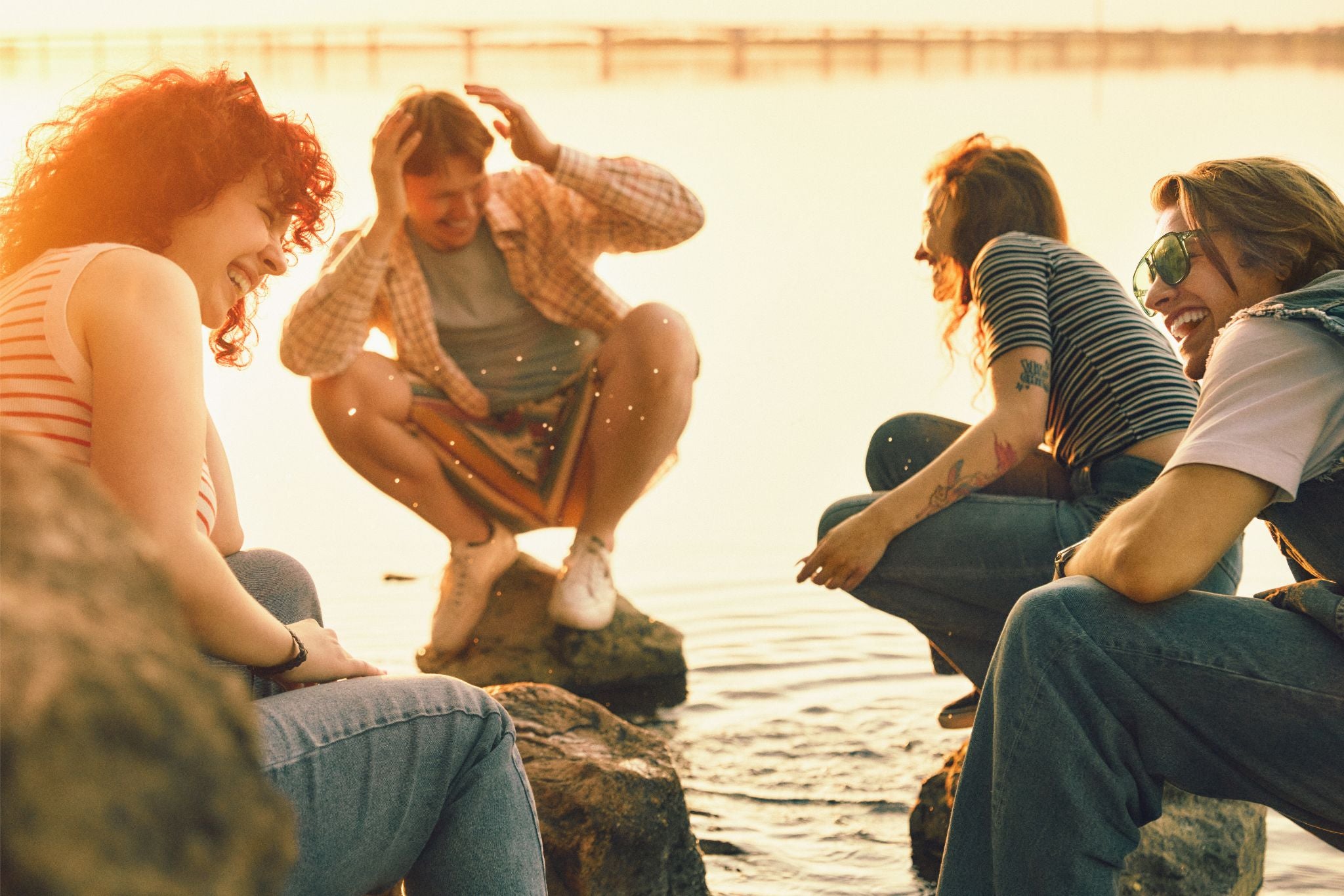 Group of friends sitting by a body of water at sunset