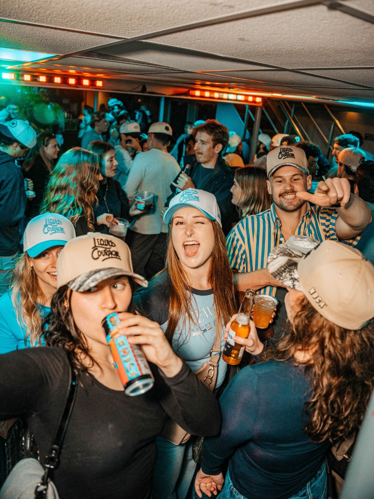 Group of people at a party with drinks, wearing casual clothing and hats.