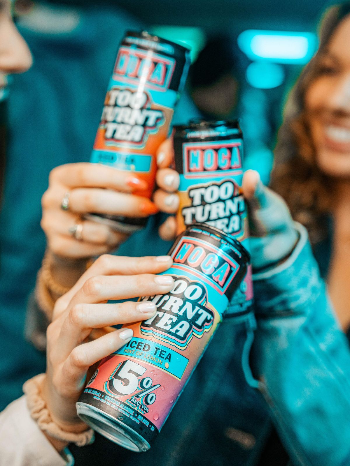 Three people holding cans of 'Too Turnt Tea' in a social setting.