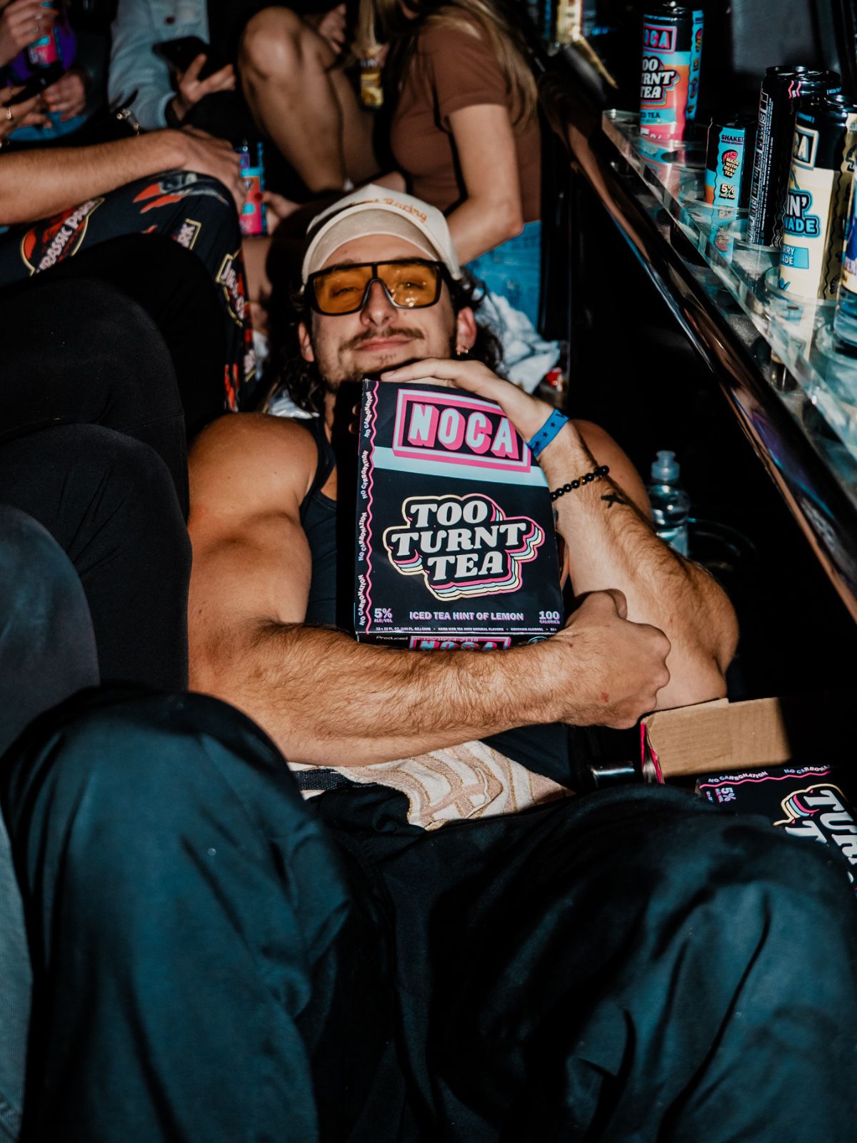 Man holding a 'Noca Too Turnt Tea' box in a bar setting