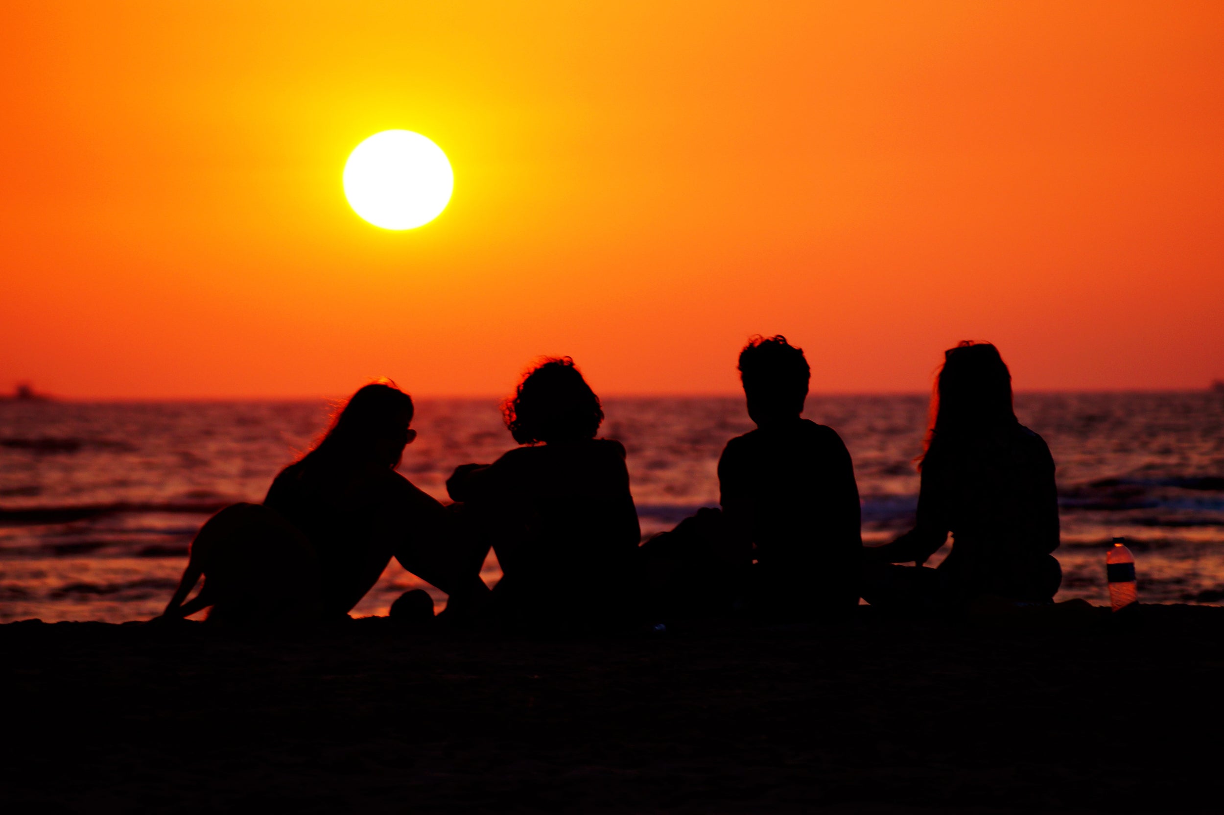 Silhouettes of people sitting on a beach at sunset.