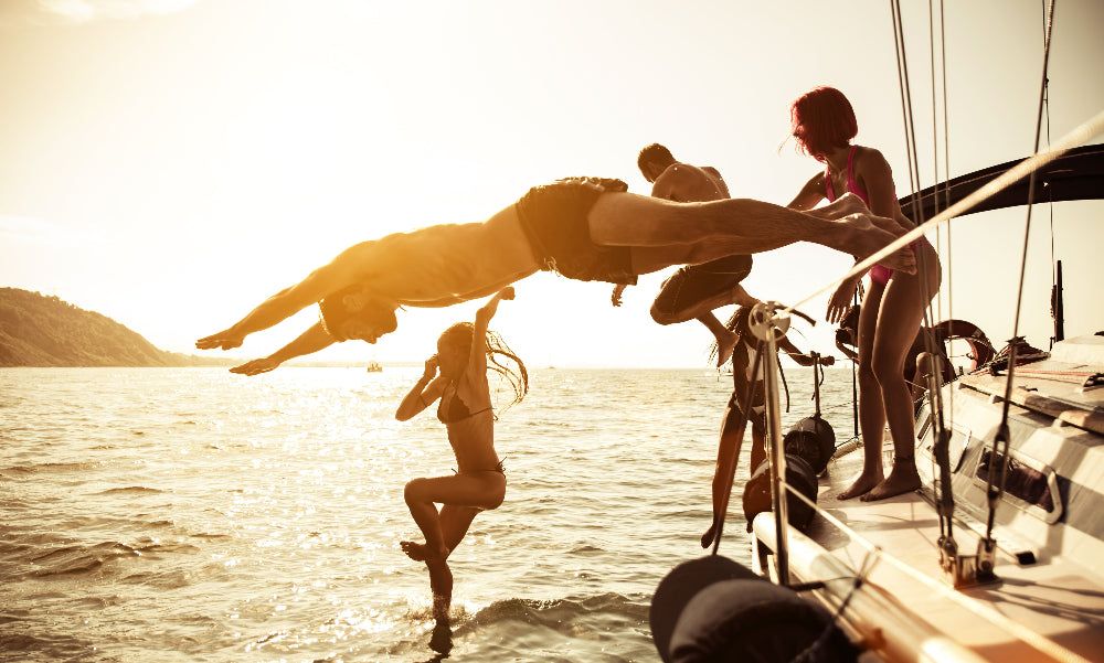 People on a boat with a man jumping into the water at sunset