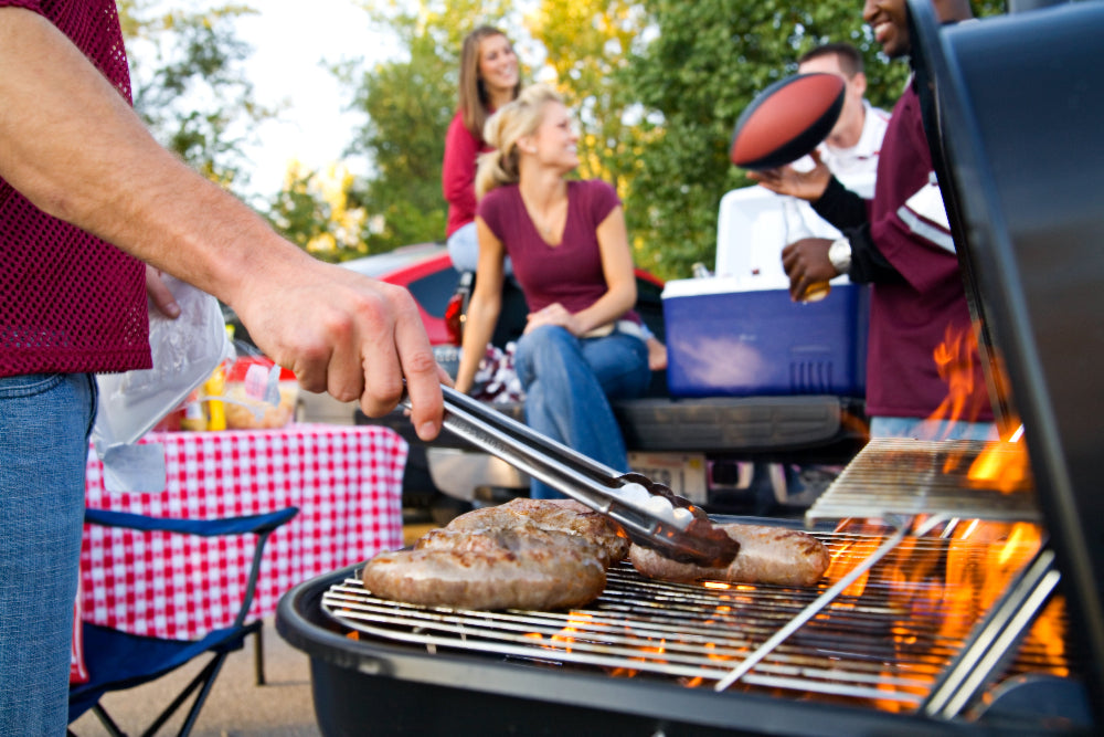 People grilling outdoors with a checkered tablecloth and cooler in the background
