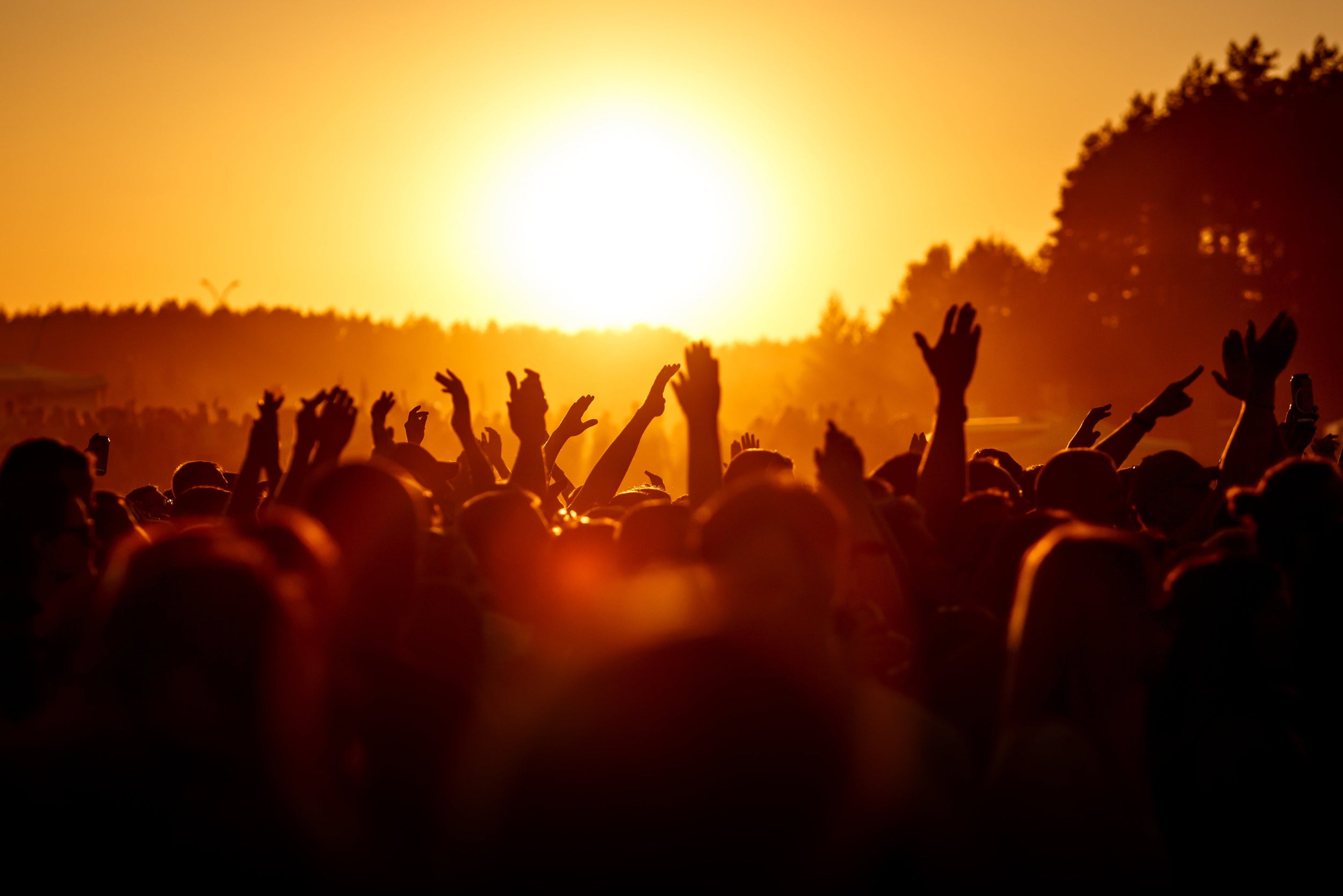 People with raised hands against a sunset sky